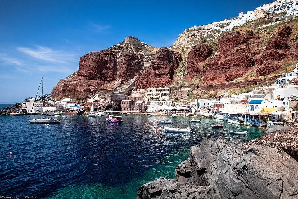 Boats in Ammoudi Bay’s little harbour below red cliffs, Oia above