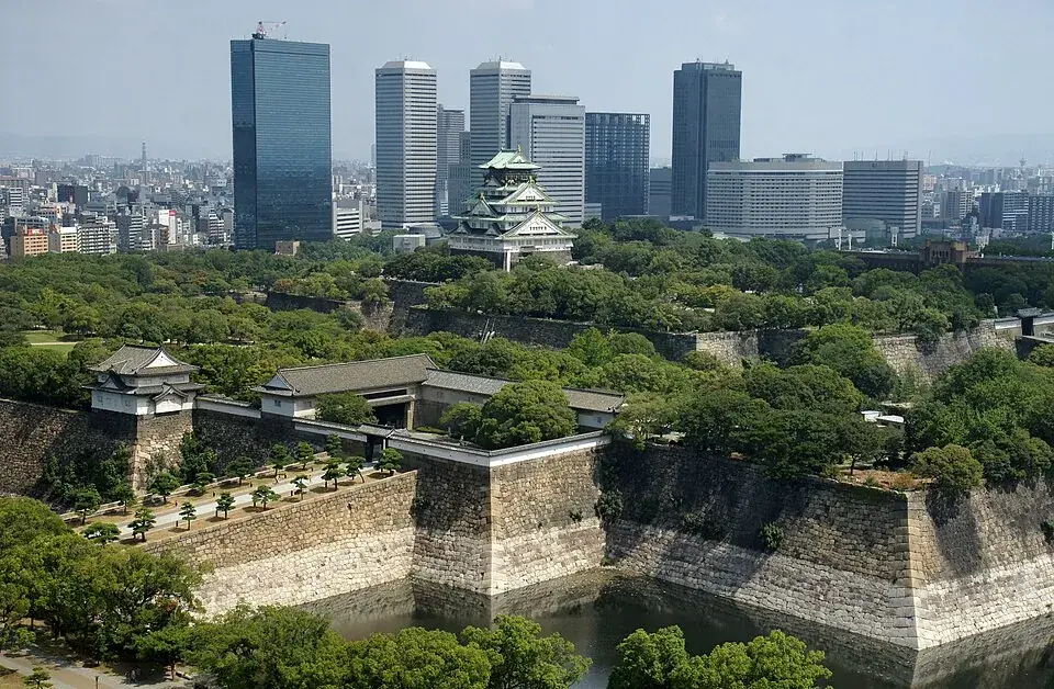 Osaka Castle’s main tower above its stone walls and moat, office towers behind